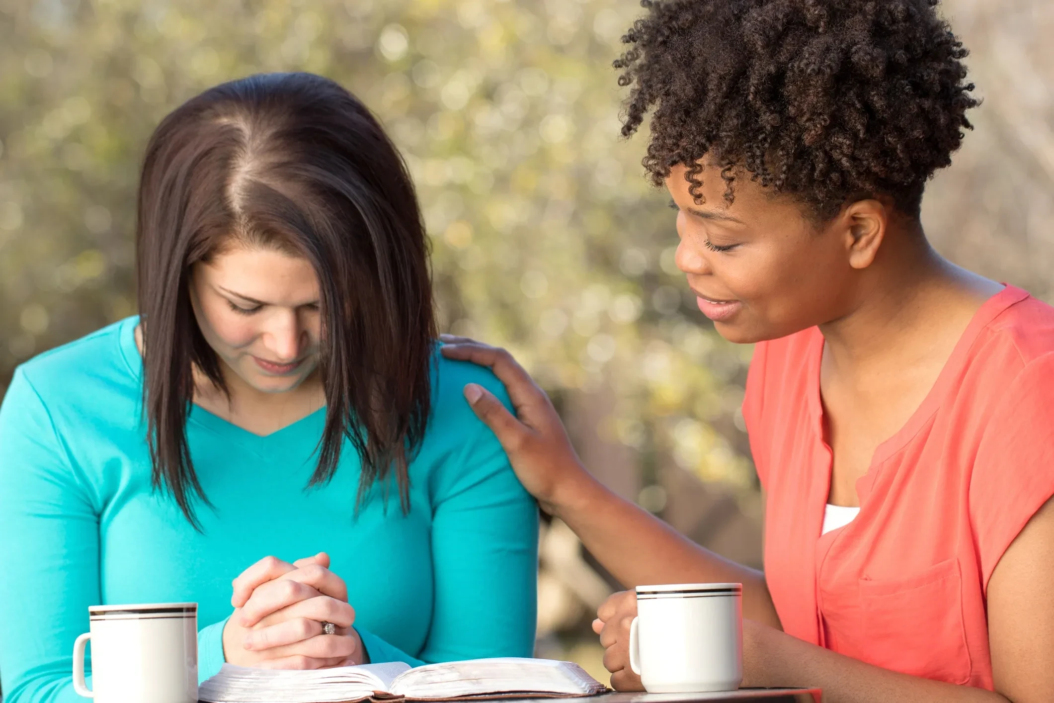 Two women praying together over an open Bible